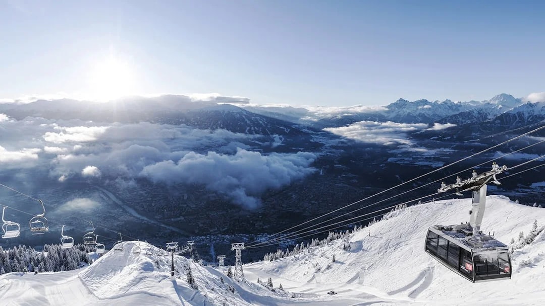 Cable car ascending snowy mountain with view of Innsbruck and Alps.