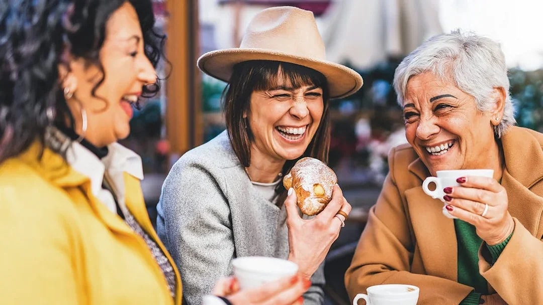 Senior women laughing at a bar, enjoying coffee and pastries.