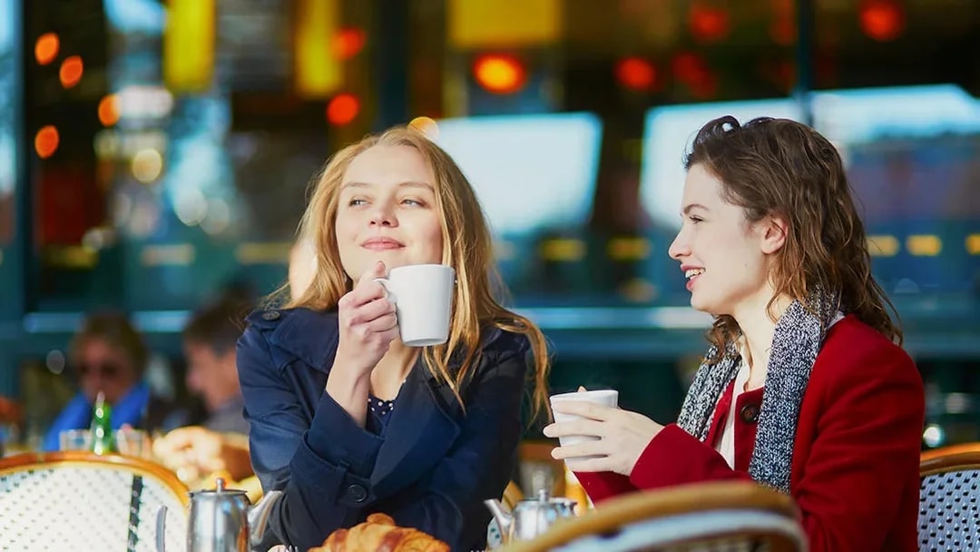 Two young girls enjoying coffee at a cafe table with croissants.