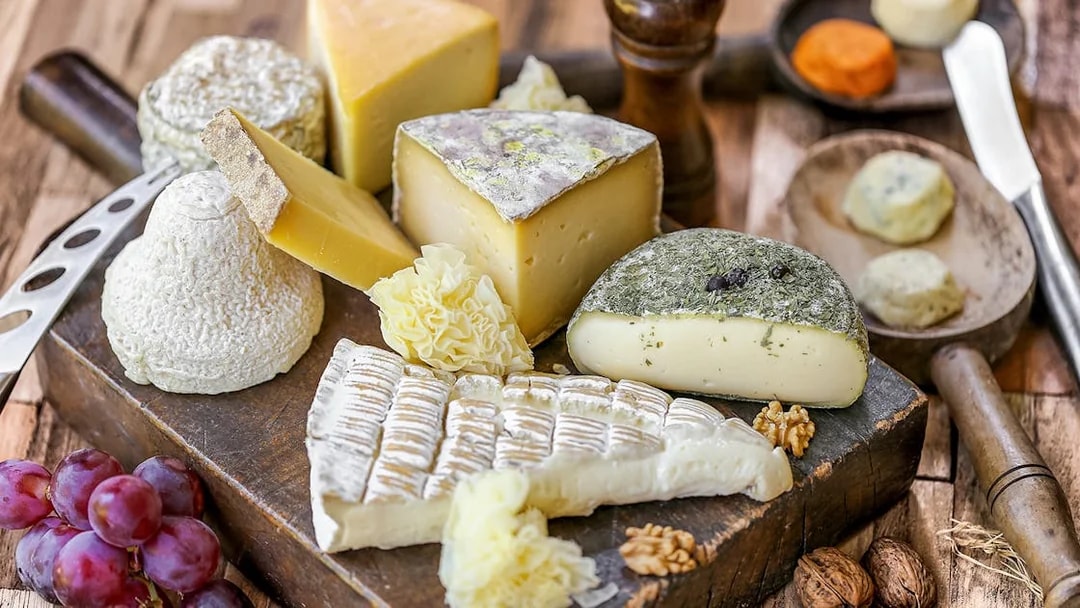 Assorted French cheeses and grapes on a wooden board, featured in Paris Saint Germain food tours.