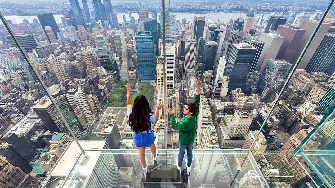 Tourists on glass floor at SUMMIT One Vanderbilt overlooking New York City skyline.