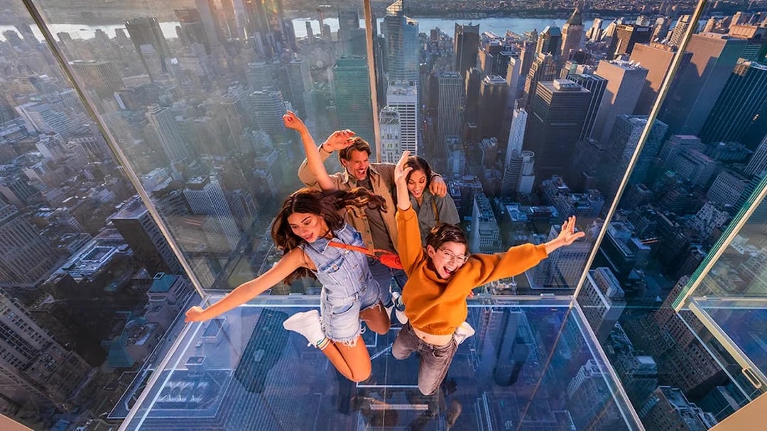 Group enjoying glass observation deck at SUMMIT One Vanderbilt, New York City skyline in background.