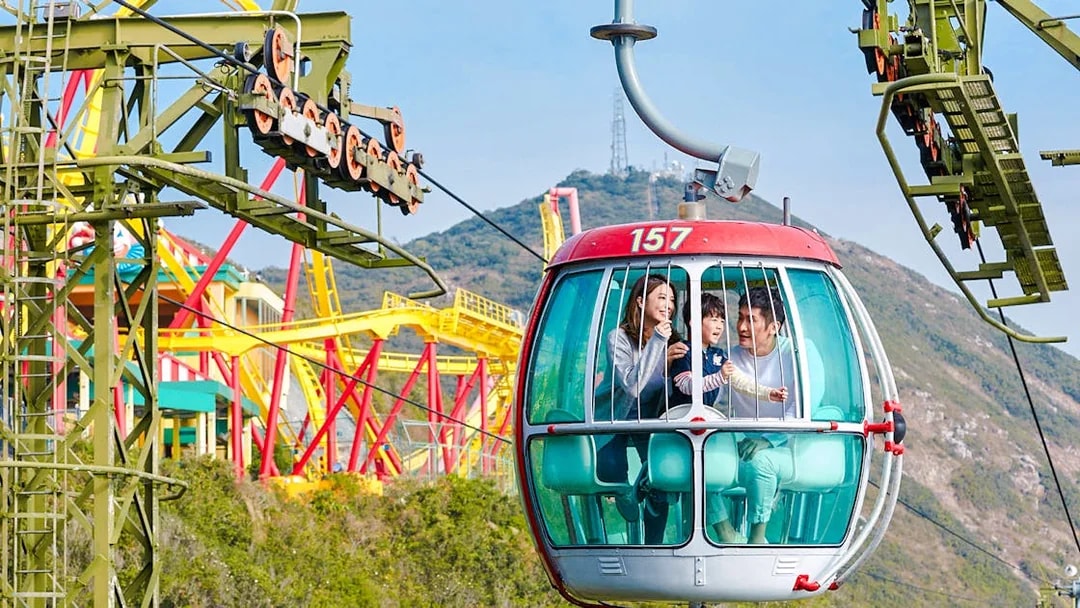 Family enjoying a cable car ride at Ocean Park Hong Kong with colorful rides in the background.