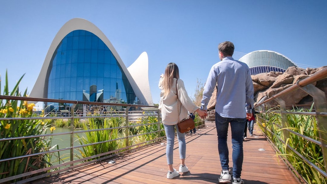 Couple walking towards Oceanogràfic Valencia, Spain, with modern architecture in view.