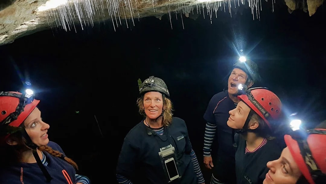 Small group exploring Waitomo Glowworm Caves with helmets and headlamps.