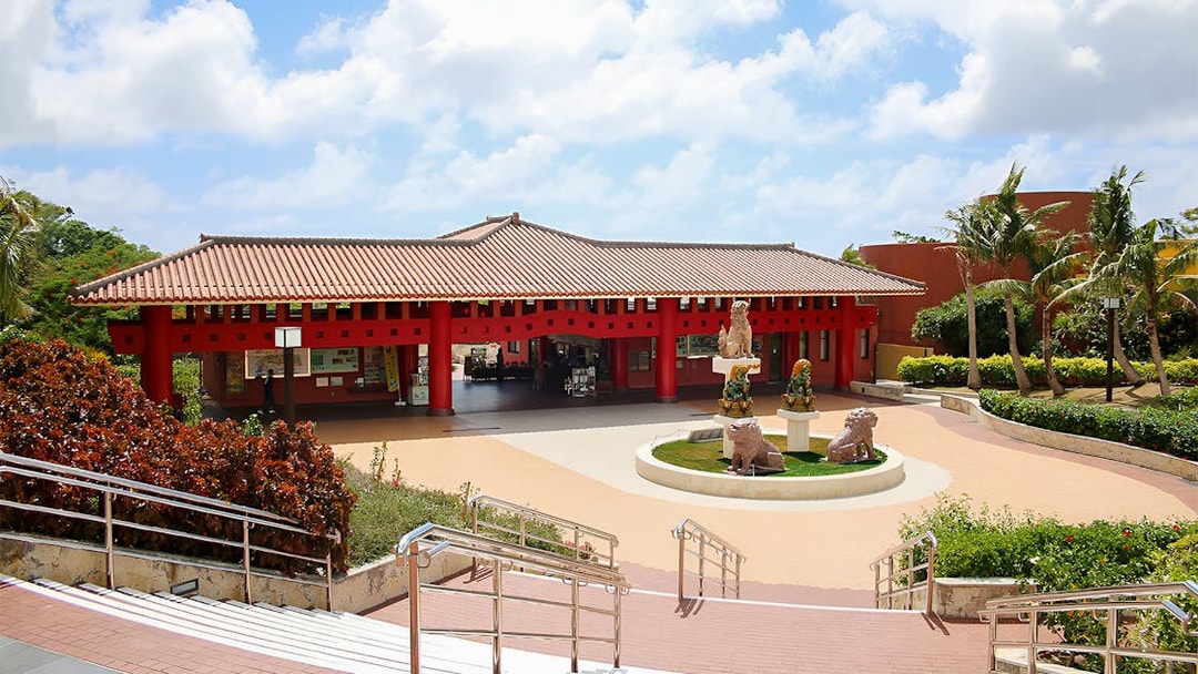 Entrance of Okinawa World with traditional red architecture and lion statues.