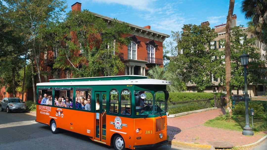 Savannah trolley with tourists passing historic brick buildings in Old Town.