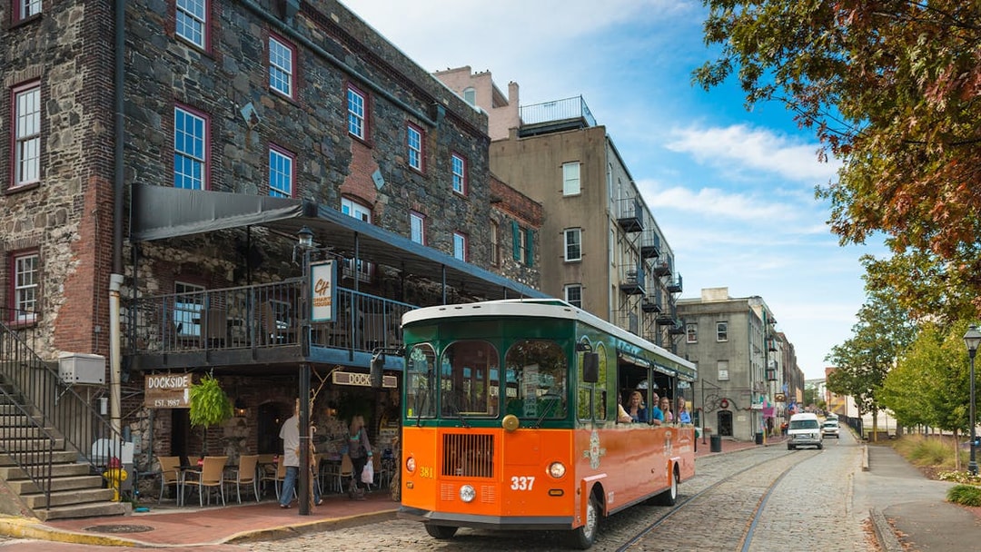 Savannah trolley on cobblestone street near historic buildings.