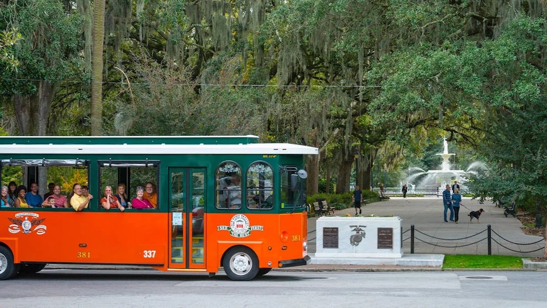 Trolley tour passing through Savannah's historic Forsyth Park with fountain in view.