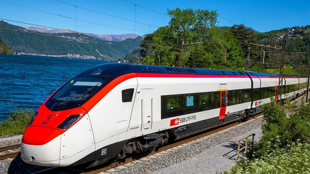 Train traveling along a scenic route near a lake, connecting Geneva Airport and Geneva Train Station.