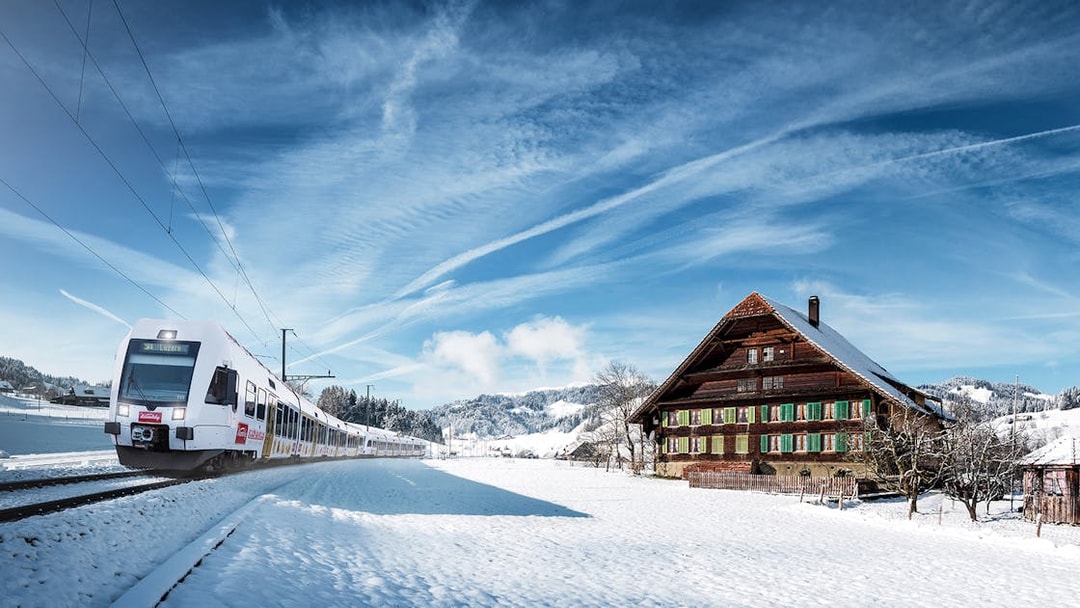Train on Lucerne–Interlaken Express passing snowy Swiss countryside with traditional chalet.