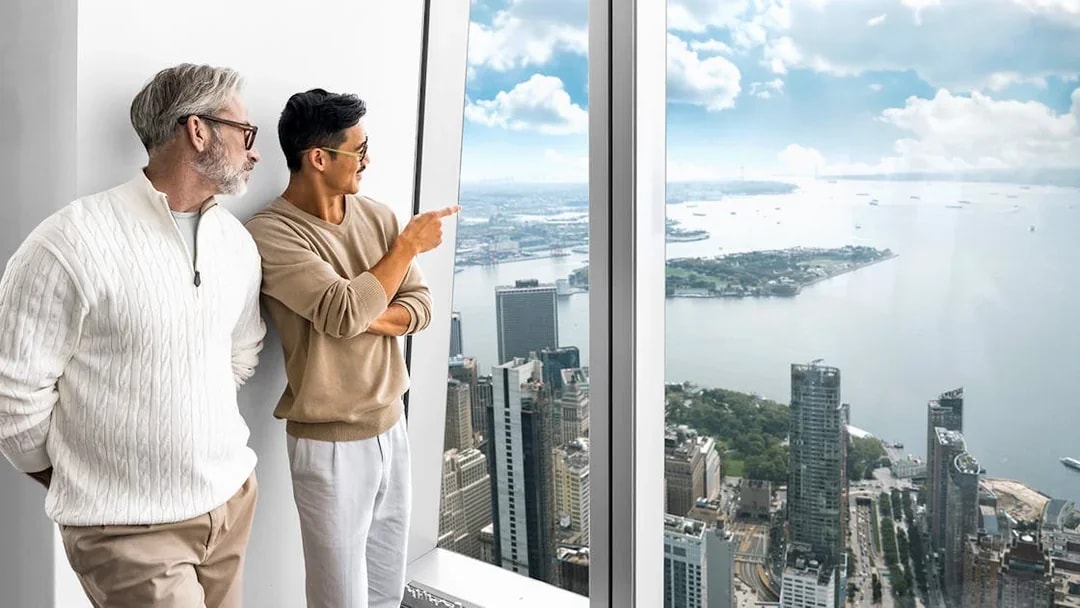 Visitors enjoying the view from One World Observatory, overlooking New York City skyline and harbor.