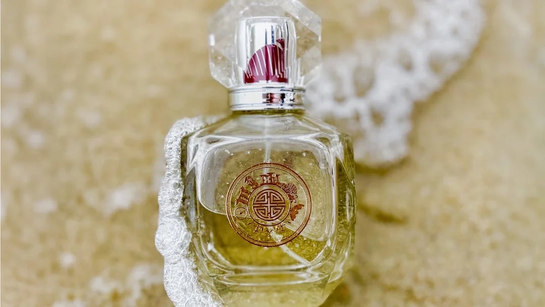 Perfume bottle with ornate design on sandy beach.