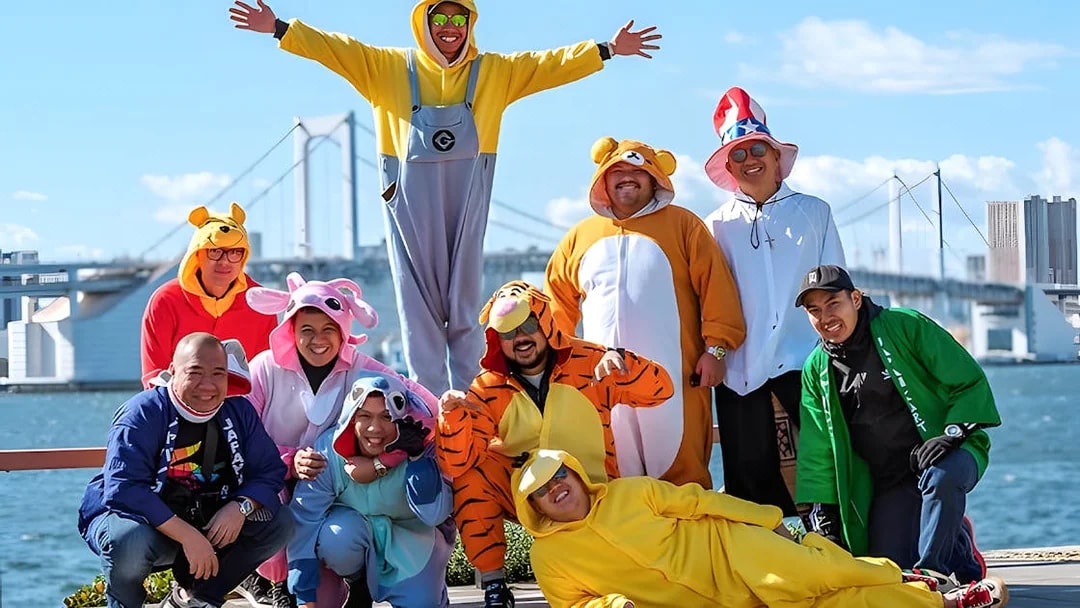 Group in colorful costumes posing by Osaka waterfront with bridge in background.