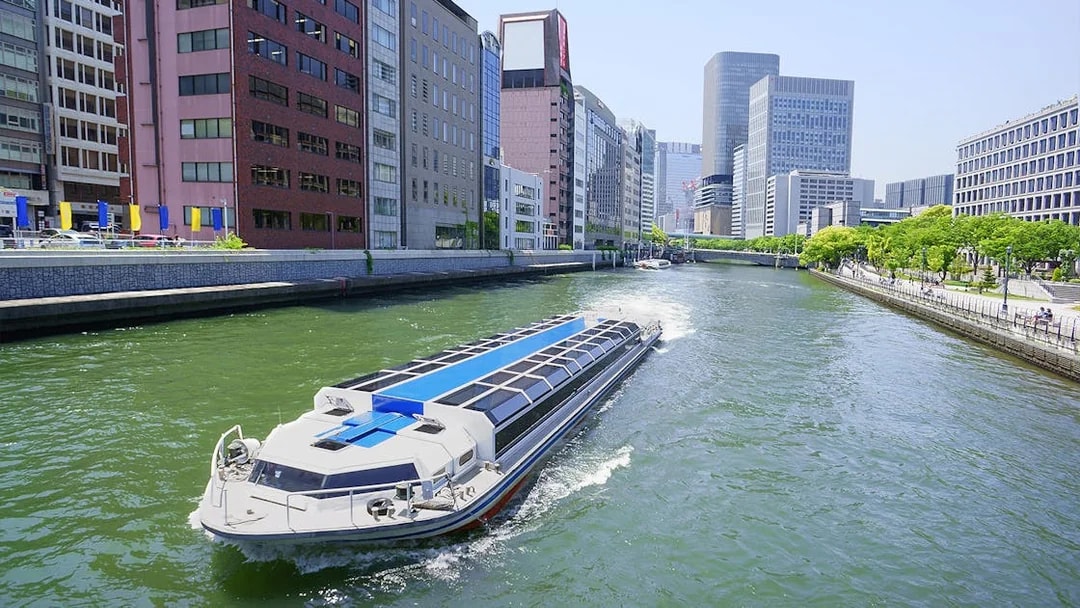 River cruise boat on Osaka canal with city skyline, part of Osaka Amazing Pass experience.