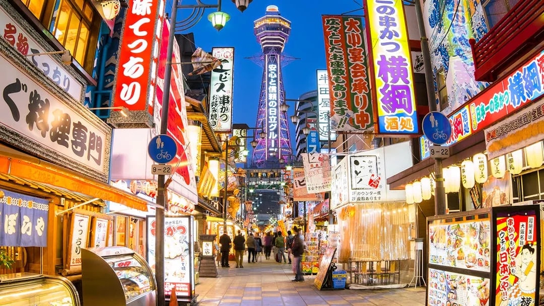 Bustling Osaka street with Tsutenkaku Tower, vibrant signs, and people exploring shops.