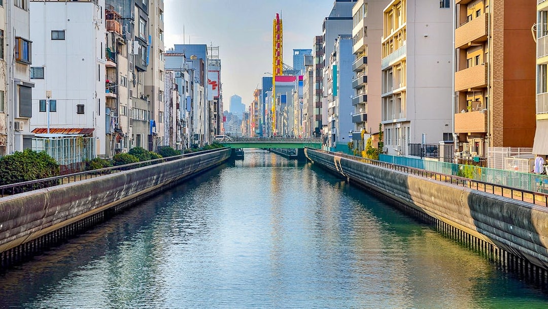 Tombori River Cruise view of Osaka's canal lined with buildings and a distant bridge.