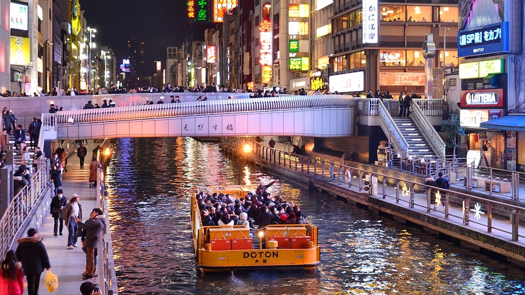 Tombori River Cruise boat passing under a bridge in Dotonbori, Osaka at night.