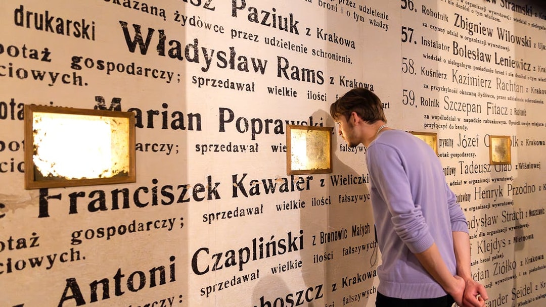 Man examining exhibit wall at Oskar Schindler's Factory museum in Krakow, Poland.