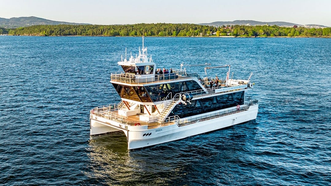 Dinner cruise boat on Oslofjord, Norway, with scenic forested shoreline in the background.
