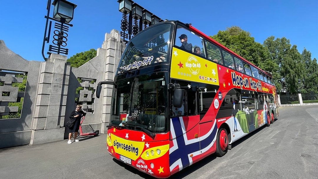 Colorful double-decker bus for Hop on Hop off tour in Oslo, parked near a stone gate.