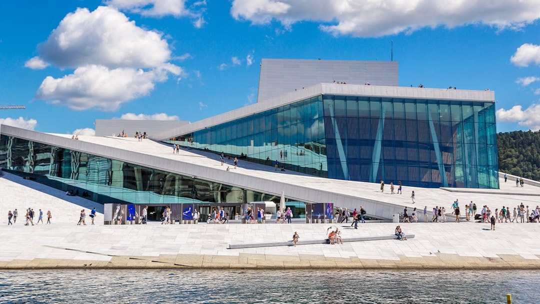 Oslo Opera House with visitors walking on its sloped roof by the waterfront.