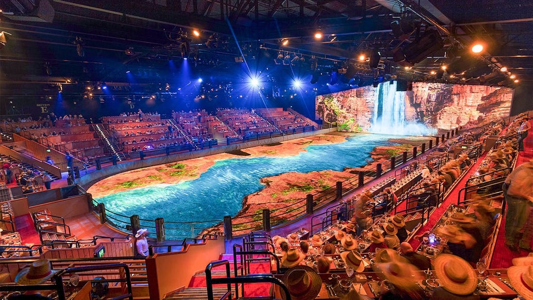 Audience watching Australian Outback Spectacular Heartland Dinner & Show with waterfall backdrop.