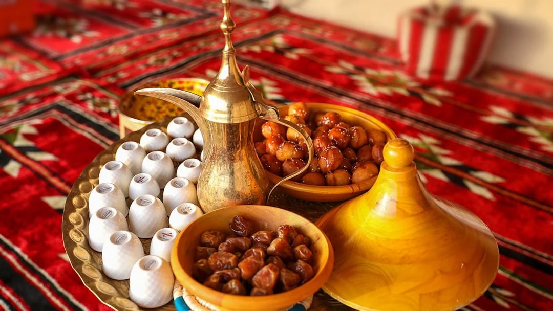 Traditional Bedouin tea set with dates and sweets on a patterned rug during desert safari.