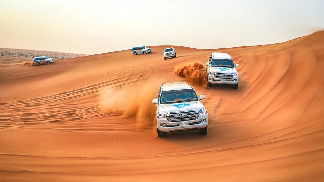 Desert safari SUVs driving over sand dunes during Bedouin desert tour.