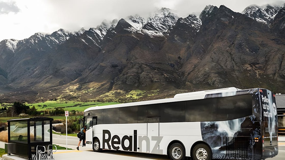 Bus at a stop with mountains in the background, Queenstown to Te Anau transfer.