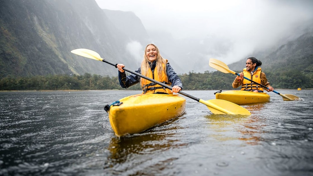 Couple kayaking in Milford Sound with misty mountains in the background.