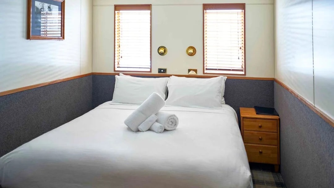 Cozy cabin bedroom with double bed and towels on an Overnight Milford Sound Cruise.
