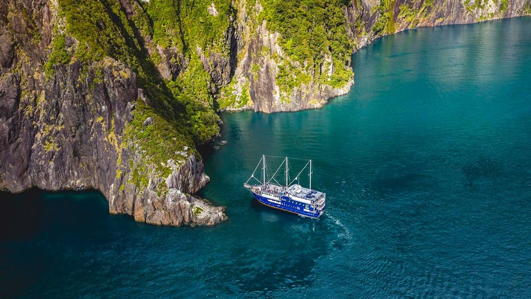 Cruise ship navigating Milford Sound's cliffs and blue waters, New Zealand.