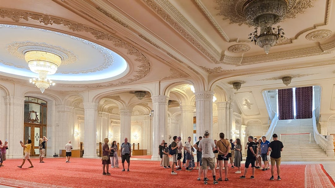 Guided tour group in the grand hall of the Palace of Parliament, near the staircase.