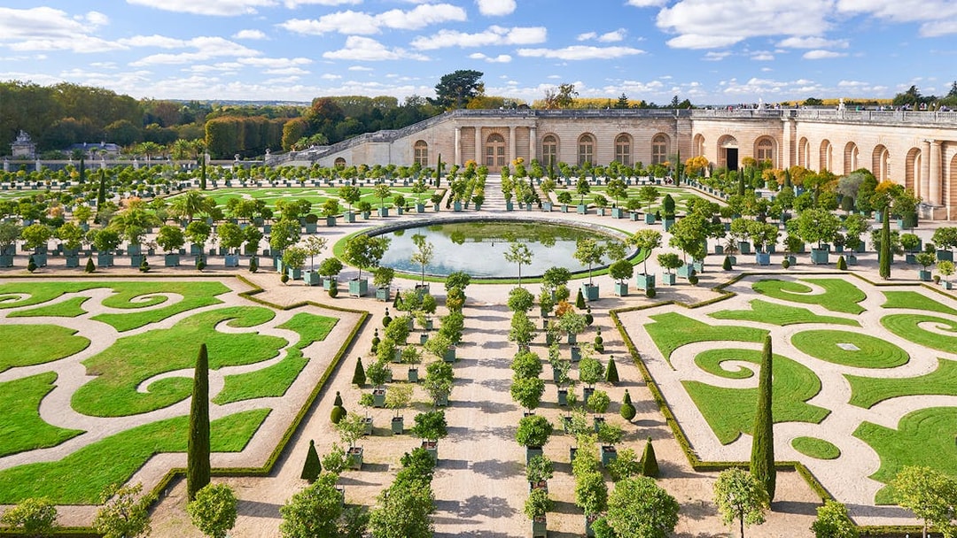 Versailles Gardens with manicured hedges and central fountain, France.