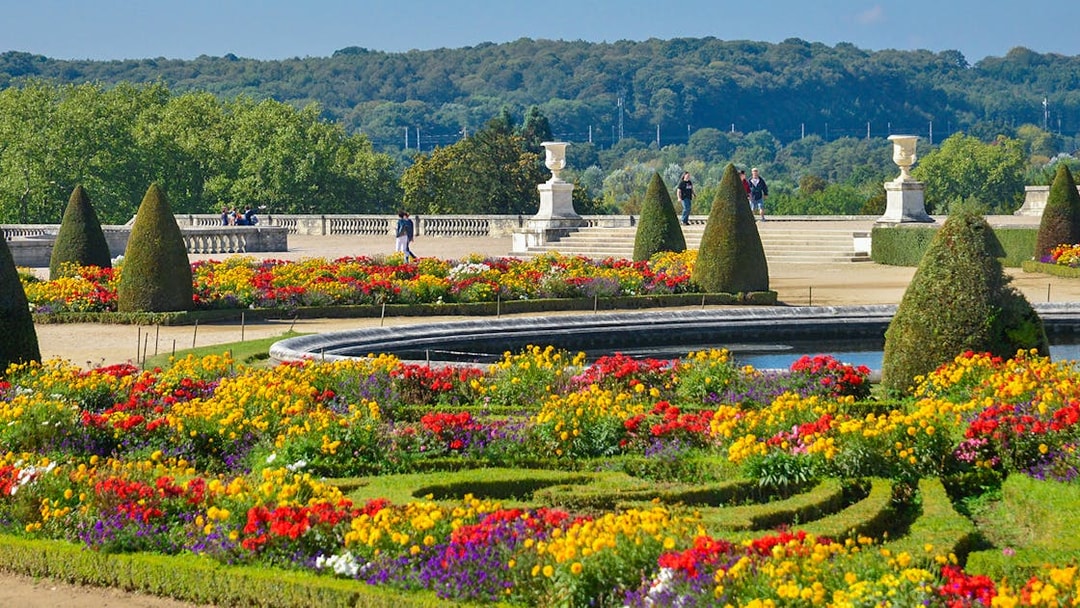 Tourists walking in Versailles Palace garden with vibrant flower beds.