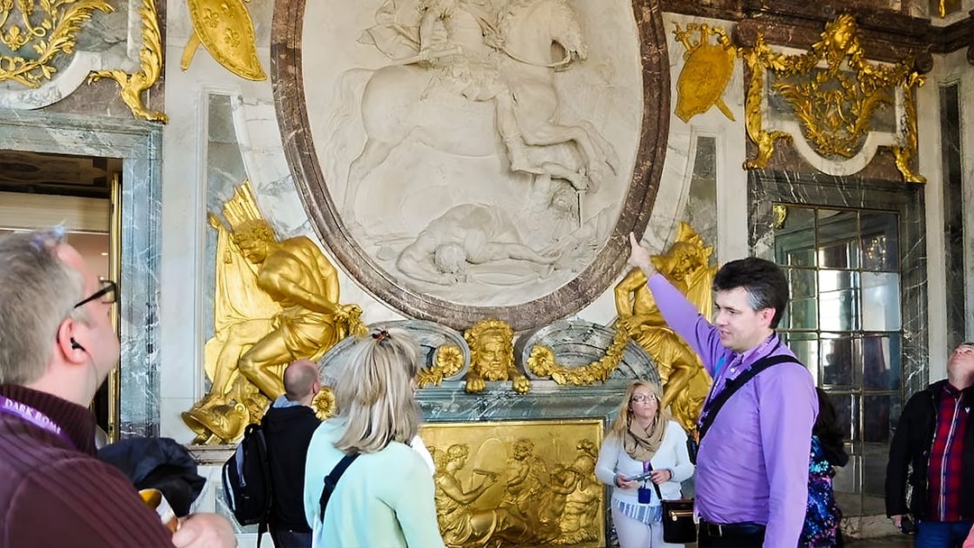 Tour guide explaining artwork inside Versailles Palace to visitors.