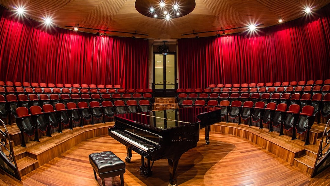 Grand piano on stage at Palau de la Música Catalana, Barcelona, with red seats and curtains.