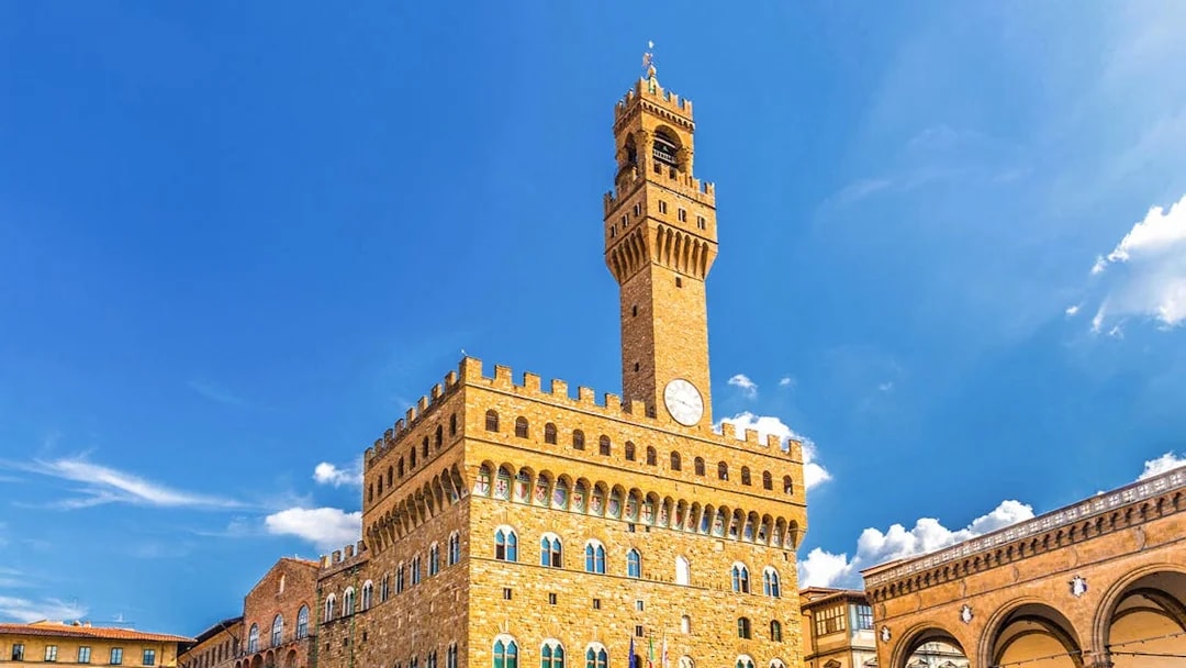 Palazzo Vecchio exterior with clock tower under clear blue sky in Florence, Italy.