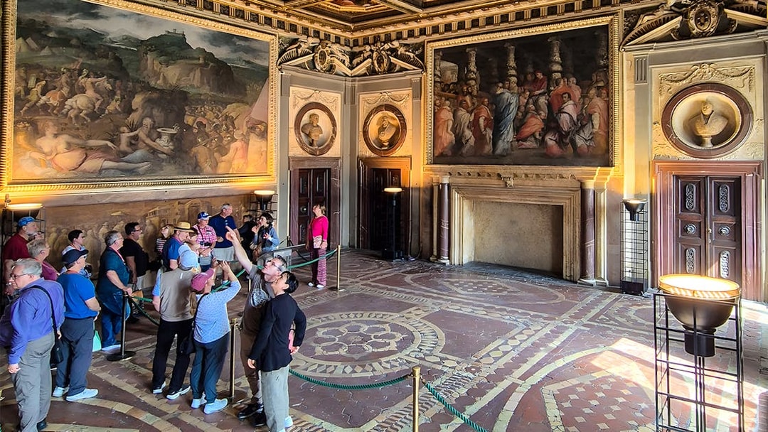 Visitors exploring the ornate interior of Palazzo Vecchio, Florence, with large frescoes on the walls.