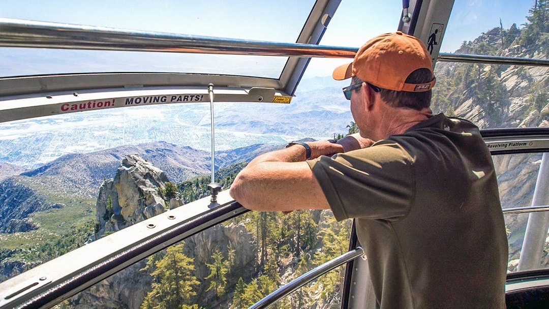 Man enjoying mountain view from Palm Springs Aerial Tramway cabin.