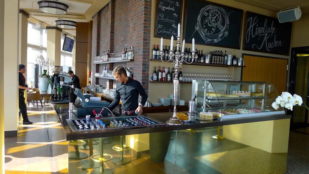 Cafe interior at Panoramapunkt Berlin with staff preparing drinks and desserts on display.