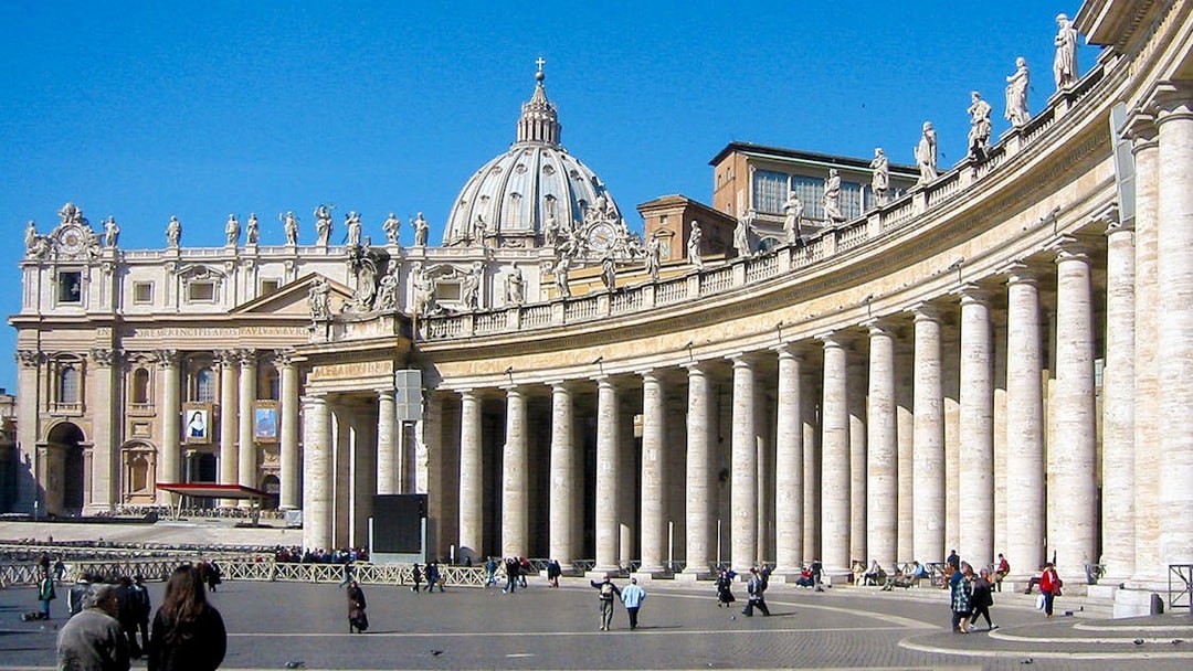 Tourists walking in St. Peter's Square with St. Peter's Basilica in Vatican City.