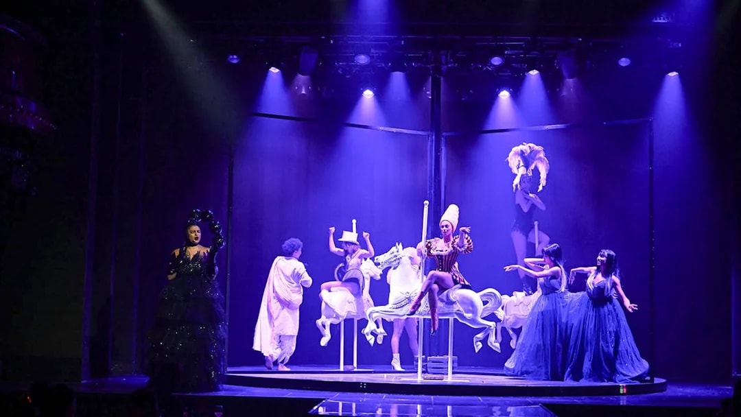 Cabaret performers on stage with carousel horses in Paris show.