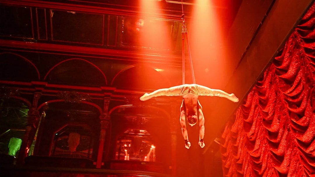 Aerial performer in Paris cabaret show, suspended upside down under red stage lights.