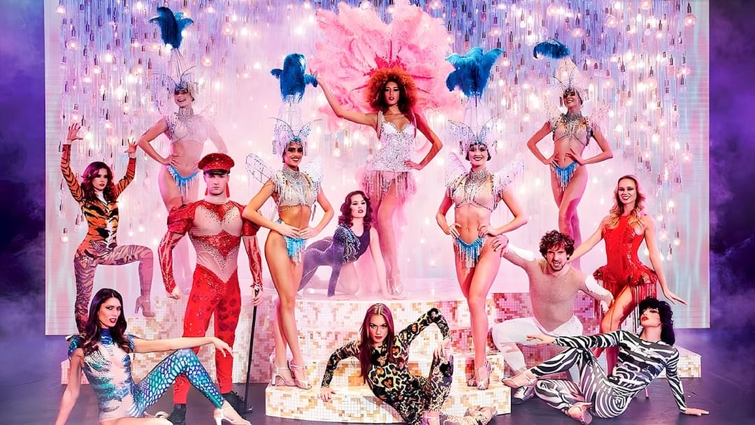 Paradis Latin show performers in vibrant costumes on stage with dinner setting.