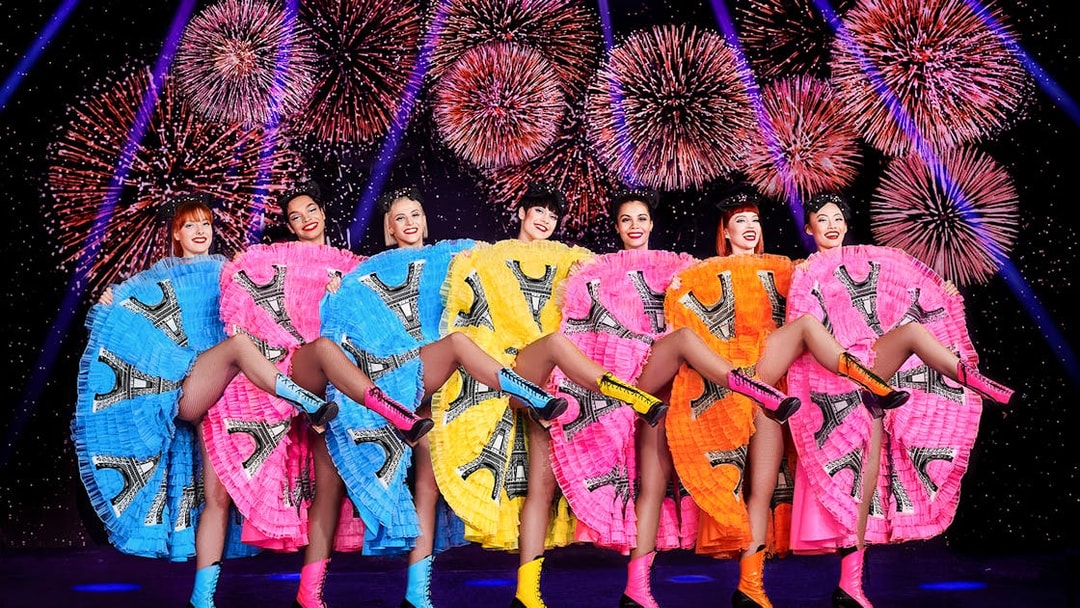 Dancers in colorful dresses performing at Pardis Latin, Paris with fireworks in the background.