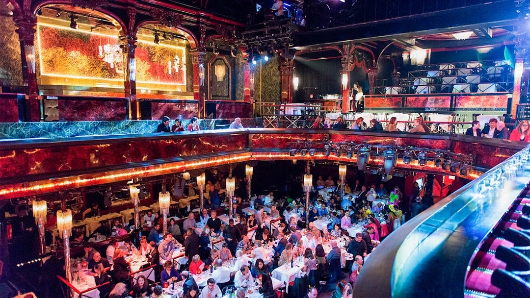 Guests dining in the vibrant hall at Paradis Latin, Paris, with ornate decor and chandeliers.