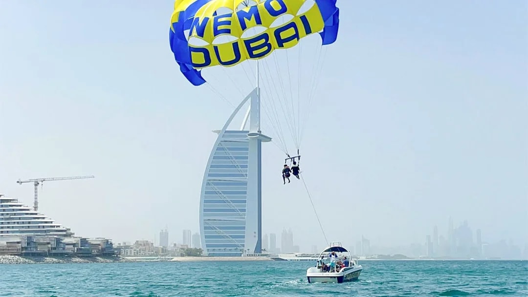 Parasailing near Burj Al Arab in Dubai with a boat on the water.