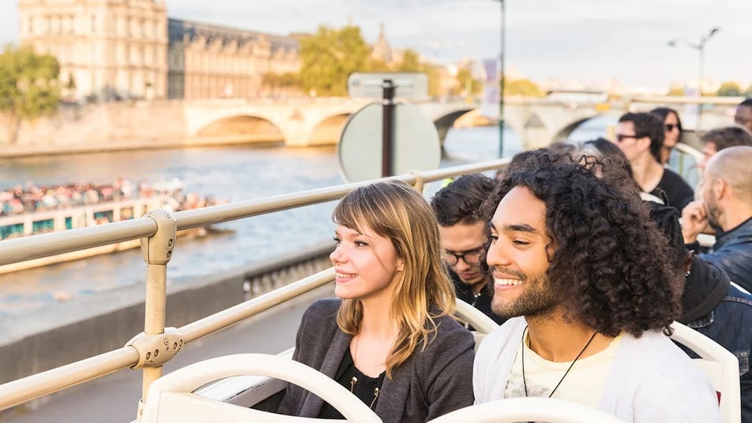 Tourists on Big Bus Paris tour with Eiffel Tower and Seine River in background.